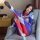 Woman in colorful superhero-themed bodysuit lounging on a gray armchair, showcasing the open-crotch design and matching sleep...