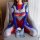 Woman wearing a colorful, form-fitting bodysuit with red, blue, and white patterns, sitting on a gray armchair. the outfit fe...