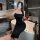 A woman poses in a bathroom wearing a black dress, holding a glass of wine, showcasing elegant evening attire.