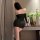 Woman in black fei niao moon gaze bodycon dress, back view, leaning on table with flowers and wine glass.