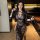Woman wearing black misty flame lace secretary sleep dress with sheer seductive design, holding a whip in modern interior.