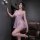Woman in sheer lavender nightgown with lace trim and bow details, posing seductively beside leather couch.