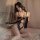 Woman wearing black flower moon seduction lingerie set with lace bodysuit, sheer cutouts and bow detail on bed.