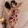 Woman in pink floral forbidden elegance lace bodysuit with fan, candles beside — modest yet sexy sleep dress & lingerie set.