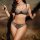 Woman wearing french-style sheer lace lingerie set with floral embroidery, black trim, and feather accessories.