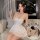 A woman elegantly poses holding a glass, wearing a delicate white cami nightdress with tie-back design, perfect for summer sl...