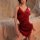 Woman wearing red velvet lingerie dress with deep v neckline and lace trim, sitting on bed.
