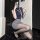 A woman poses in a navy blue top and gray mini skirt, wearing black stockings and high heels. the outfit features an id badge...