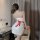 A woman wears a white nurse costume with a red bow, standing by a desk holding a whip, ideal for cosplay at nightclubs or par...