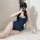 A woman poses in a navy blue one-piece swimsuit with white trim, sitting on a fluffy rug against a white door background. the...