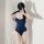 A woman poses in a navy blue one-piece swimsuit with white trim, capturing her reflection in a mirror. the design features a ...