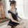 A woman sits on a fluffy rug wearing a navy blue sailor uniform dress with white trimmings, featuring a bow and pleated skirt...