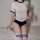 A woman wears a white and navy japanese gymnastics outfit with thigh-high socks, posing on a bed. the set features playful de...