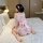 A woman sits on a bed wearing a sheer pink japanese kimono-style sleepwear set, featuring floral patterns and a large bow at ...