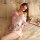 A woman lounges on a bed wearing a delicate pink japanese kimono sleepwear set, featuring floral patterns and sheer mesh fabr...