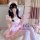 A girl wearing a cute japanese maid dress with pink and white colors, featuring ruffles and bows. she holds a teacup while si...