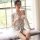 A woman sits by a window wearing a sheer lace sleepwear set, featuring a delicate floral pattern. the outfit includes a tie-f...