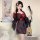 A woman poses elegantly in a japanese-style kimono set, featuring black fabric with floral embroidery and a red sash. she hol...