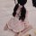 A person sits on a bed wearing a pink japanese-style sleepwear set featuring cute bunny and maid details, creating a playful ...