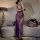 A woman poses in a sheer purple lace dress, highlighting its elegant design and see-through fabric. the bodice features delic...