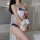 A woman models a lace bikini set featuring a sailor-style design with blue accents and a red bow detail, holding a plush rabb...