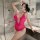 Woman wearing a vibrant pink lace bodysuit with an open-crotch design, posing seductively in a modern bathroom setting.