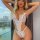 Woman wearing white luxury lace bodysuit – sheer, sexy european-style lingerie with floral details and bow accents.
