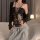 Woman wearing black lace cami bodysuit with bind-up front, paired with gray sweatpants and cardigan, holding glass.