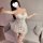 Woman wearing a white lace halter bodycon mini dress with satin accents and matching thigh-high stockings, posing indoors.