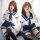 Two women wearing matching sailor-style outfits with bows, sailor skirts, and striped stockings pose playfully indoors.