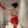 Woman wearing red lace love chain lingerie set with sheer mesh, long gloves, and garter straps in a modern bathroom.