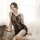 Woman wearing black lace mesh babydoll sleep set with sheer floral embroidery, posing on fluffy rug in soft light.