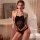 Woman modeling black lace bodysuit set with open-crotch design, sheer fabric, and elegant straps in soft-lit bedroom setting.