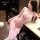 Woman modeling pink lace bodysuit with sheer bust, bows, and matching garter stockings in elegant bedroom setting.