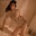 Woman in lace sheer mini bra set and silk-like qipao sleep dress, vintage-inspired lingerie on bed with fan.