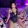 Woman wearing black lace sheer open-crotch bodysuit with cat ears, lying on bed scattered with red rose petals under purple l...