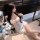 Woman in white lace sheer sleep dress with blue bows, sitting beside flowers and balloons.