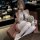 A woman poses elegantly in a white maid costume, featuring sheer stockings and lace details. she holds a plush teddy bear whi...