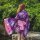 A woman stands by a pond wearing a purple lolita dress with cherry blossom patterns, featuring a pink ribbon belt and flowing...