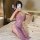 A woman poses on a bed wearing a purple lace long dress, featuring sheer fabric and floral patterns. she holds a fan accessor...