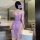 A woman stands facing away from the camera, wearing a purple lace long dress with sheer fabric and floral patterns. the desig...