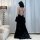 A woman stands facing away from the camera, wearing a black lace gold velvet embroidered long sleep dress with a backless des...