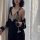 A woman wears a black lace gold velvet embroidered long sleep dress with backless design and tie belt robe set, holding a win...