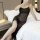 A woman wearing a sheer black sleep dress with spaghetti straps, sitting on a bed holding a cup. the dress features lace deta...