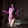 Woman wearing purple night charm lingerie set, sheer mesh bodysuit with lace cutouts and long sleeves, posing in dimly lit ro...