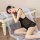 A woman lounges elegantly on a bench wearing a sheer black lace sleepwear set, featuring delicate ruffles and a flowing veil,...