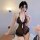 Woman wearing black lace mesh long night lingerie set with pearl necklace, sitting on bed beside pink roses.