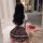 A woman sits on the floor wearing a plaid skirt and white top, holding a bouquet of roses, in a stylish room setting. the out...