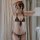 Woman wearing black sheer lace lingerie set with tie-strap babydoll top and matching thong, elegant bedroom styling.