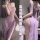 Woman modeling a purple lace cheongsam dress with an off-shoulder neckline, high slit, sheer fabric, and backless cutout desi...